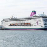 Imagen de un crucero en el mar con pasajeros en la cubierta, algunos de ellos con mascarillas
