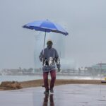 Imagen de lluvias intensas en una calle con paraguas y agua corriendo por la calzada
