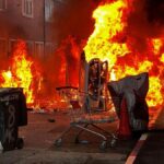 Imagen de una calle de Belfast con vehículos y viviendas dañados por el fuego tras las protestas violentas