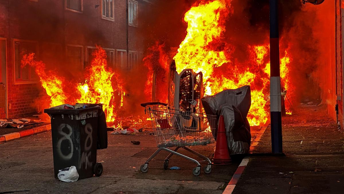 Imagen de una calle de Belfast con vehículos y viviendas dañados por el fuego tras las protestas violentas