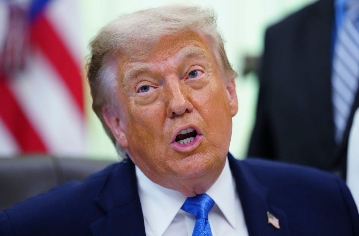 Donald Trump hablando en un podio con banderas de Estados Unidos detrás, sonriendo tras anuncio de suspensión de ataques a Irán